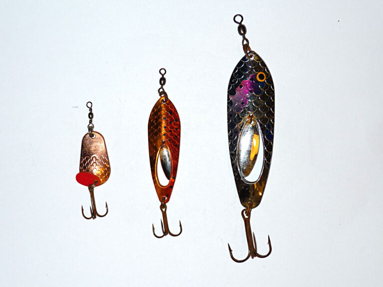 Drei unterschiedlich große Fischköder mit Drillingen auf weißem Hintergrund, ideal für das Angeln auf verschiedene Fischarten. Die Köder haben metallische Oberflächen mit glitzernden Farben.